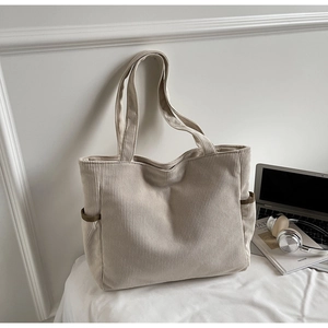 Close-up of beige corduroy tote bag showing vertical texture and side pocket detail