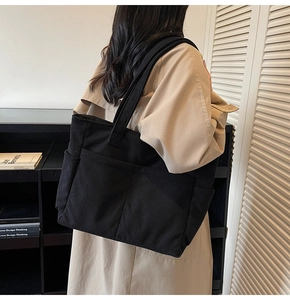 Close-up of black corduroy tote bag with multiple outer pockets shown on model's shoulder