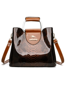 Detail of glossy snakeskin pattern handbag with metal handle and golden logo
