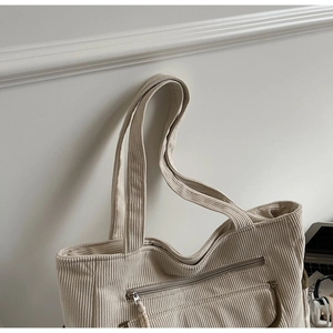 Close-up of off-white corduroy tote bag showing vertical ribbed texture and zipper pocket