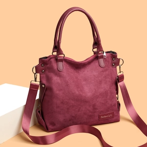 Large burgundy suede tote bag with leather handles and adjustable strap on a minimalist base