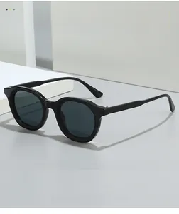 Close-up of polished black oval sunglasses with dark lenses on a minimalist geometric background