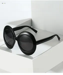Close-up of oversized oval sunglasses featuring glossy black frames and dark lenses