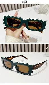 Detail of irregular serrated sunglasses with dark green frames and amber lenses