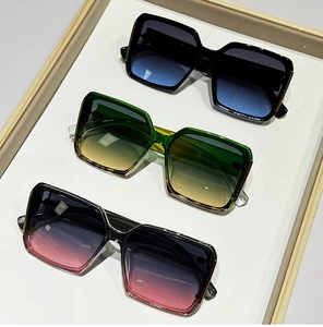 Three square sunglasses in black, green, and grey with gradient lenses on a wooden tray