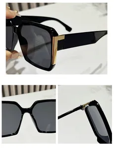 Close-up of black square sunglasses with gold metal hinge detail and grey lenses