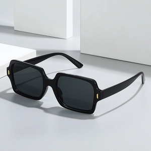 Retro square black sunglasses with dark lenses and gold hinge accents on white blocks