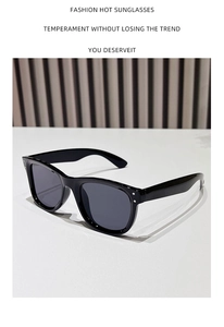 Detail view of black oversized fashion sunglasses with silver dot accents on a wood background