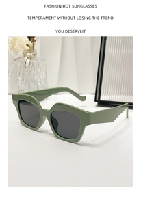 Detailed view of trendy green thick-frame sunglasses with dark lenses on a white surface