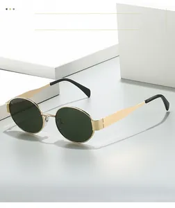 Detail of oval sunglasses featuring gold metal frame and dark green lenses on white stand