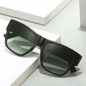 Lunettes de soleil noires modernes avec verres vert foncé sur un support blanc