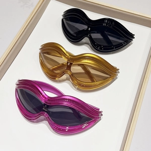 Y2K wavy lip-shaped oversized sunglasses in black, amber, and pink displayed on a tray
