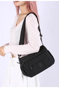Side view of multi-compartment black nylon crossbody bag on a model showing side profile