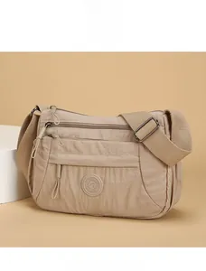 Close-up of beige nylon crossbody bag featuring multi-layer zipper pockets and adjustable strap