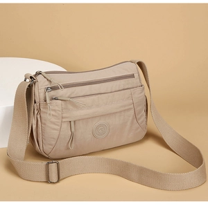 Detail view of beige nylon crossbody bag with multiple zip compartments and adjustable strap