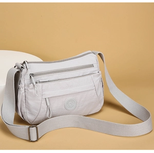 Detail view of the light grey nylon cross-body bag featuring three multi-zip compartments