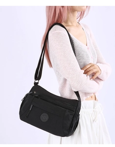 Close-up of lightweight black nylon crossbody bag with multi-zipper pockets on model