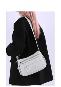 Detail showing multi-zipper compartments on light grey nylon crossbody shoulder bag