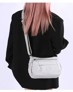 Rear view of a light gray nylon crossbody bag featuring multiple zipper compartments