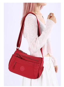 Close-up of red nylon shoulder bag featuring multiple zippered pockets and round logo