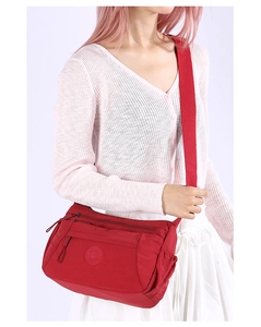 Detail view of a red nylon crossbody bag with multiple zippers shown on a model
