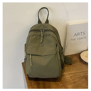 Détail du sac à dos en nylon vert olive avec logo métallique rond et tirettes de zip tissées
