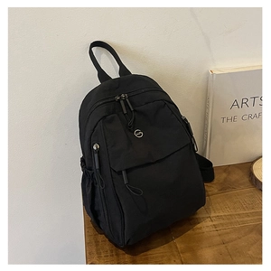 Détail du sac à dos noir en nylon avec logo métallique et poche à rabat sur un bureau