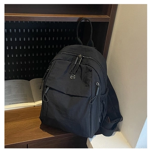 Détail du sac à dos en nylon noir avec poche zippée avant et écusson de logo circulaire