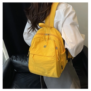 Détail d'un sac à dos léger en nylon jaune vif avec un emblème de logo en métal rond