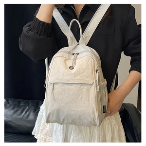 Détail du sac à dos en nylon crème montrant la texture plissée et l'étiquette de marque