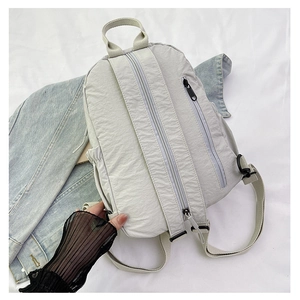 Vue détaillée du sac à dos en nylon gris clair sur tissu denim montrant fermetures et sangle
