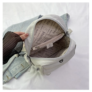 Détail d'un sac à dos en nylon crème montrant la poche zippée et la doublure logo