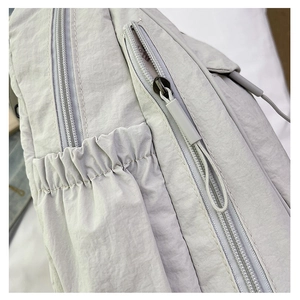 Détail d'un sac à dos en nylon gris clair avec double fermeture et poche latérale
