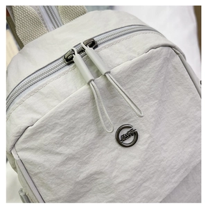 Détail du tissu en nylon beige du sac à dos, logo métallique et tirettes de fermeture