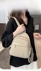 Detail of a beige mini nylon backpack showing multi-zipper pockets and brand label on strap