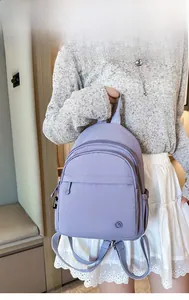 Model holding a purple nylon backpack with front zipper pockets and woven side straps