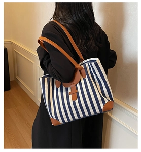 Blue and white striped canvas tote bag with brown leather handles shown on a shoulder