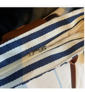 Detail of silver metal zipper closure and brown leather handles on striped canvas tote