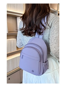 Rear view of a model wearing a purple lightweight nylon backpack in a minimalist setting
