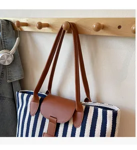 Detail of blue and white striped tote bag with brown leather handle hanging in cozy setting