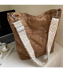 Détail du sac matelassé marron avec broderie nœud blanc et bandoulière tissée ondulée