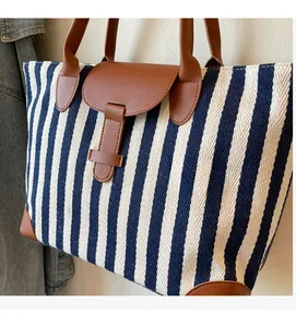 Detail of blue and white striped canvas tote bag with brown leather handles and base