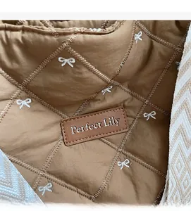 Détail du tissu matelassé marron avec broderie de nœud blanc et écusson en cuir