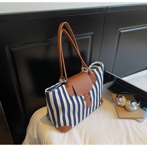 Detail of blue striped canvas tote bag with brown leather straps on a white bed