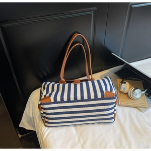 Detail of blue and white striped tote bag with brown leather handles on a bed