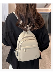 Detail of a beige mini nylon backpack with zipper compartments shown on a model