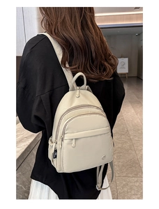 Detail view of a beige multi-layer mini backpack worn by a model in a modern interior