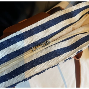 Detail of silver zipper closure on blue and white striped canvas tote with brown leather strap