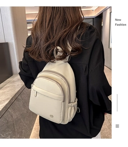 Detail of cream mini backpack showing multi-zipper pockets and elastic side pocket