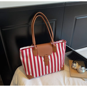 Detail of red striped canvas tote bag with brown leather handles and laptop accessory